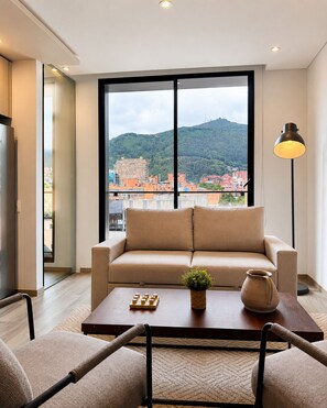 A modern living room with a sofa, coffee table, and chairs, a large window with a city view, and a floor lamp. -  Casa Indigo Apartahotel Parque 93 (Bogotá)