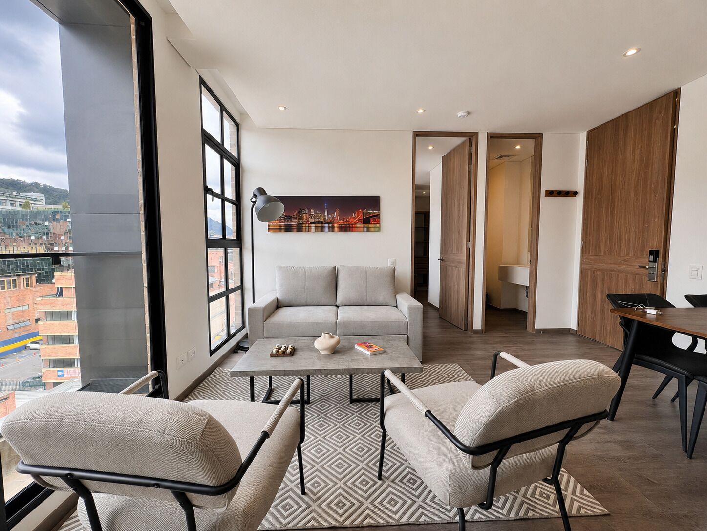 A modern living room with a sofa, two armchairs, a coffee table, and a cityscape painting.