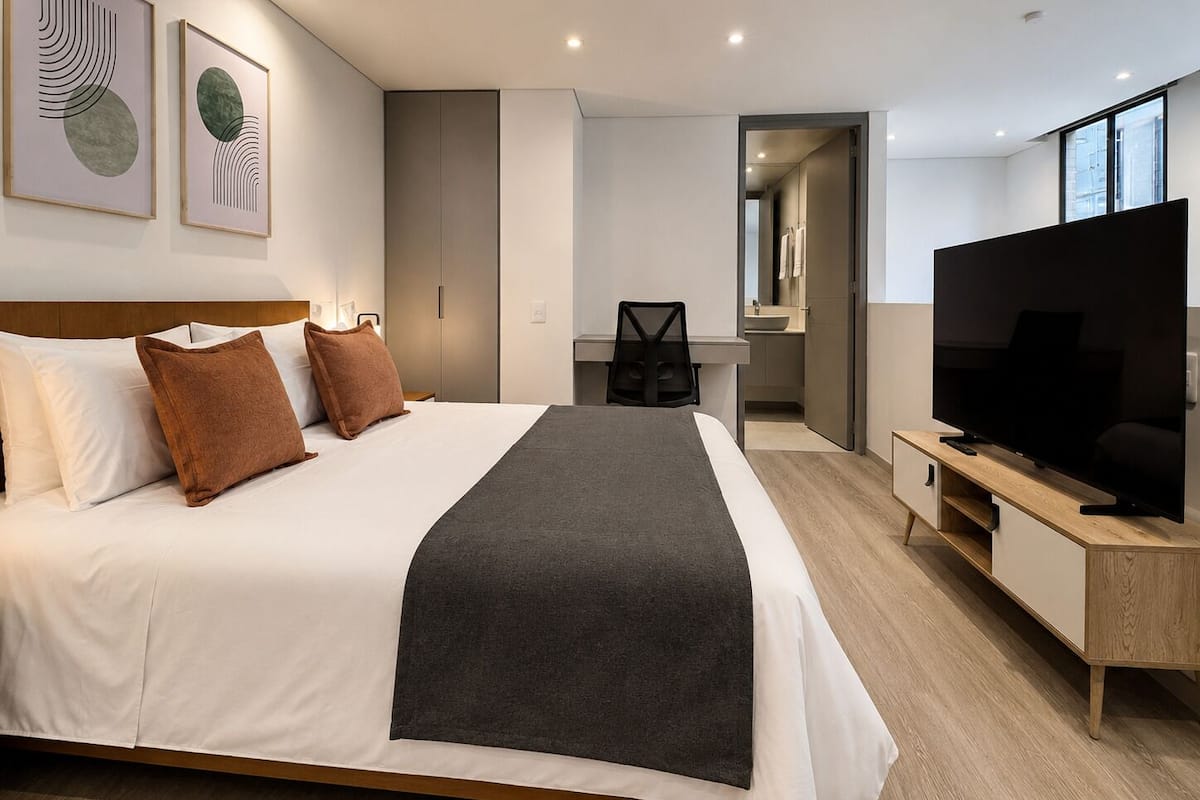 A modern hotel room with a large bed, a TV, and a desk.