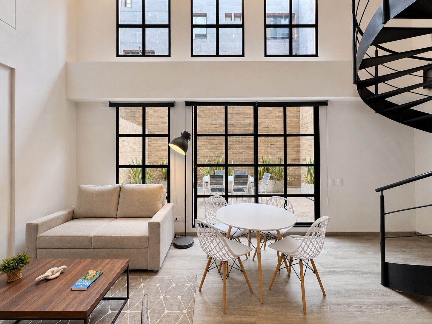 Un intérieur moderne avec un canapé, une table à manger, des chaises, une lampe et de grandes fenêtres.