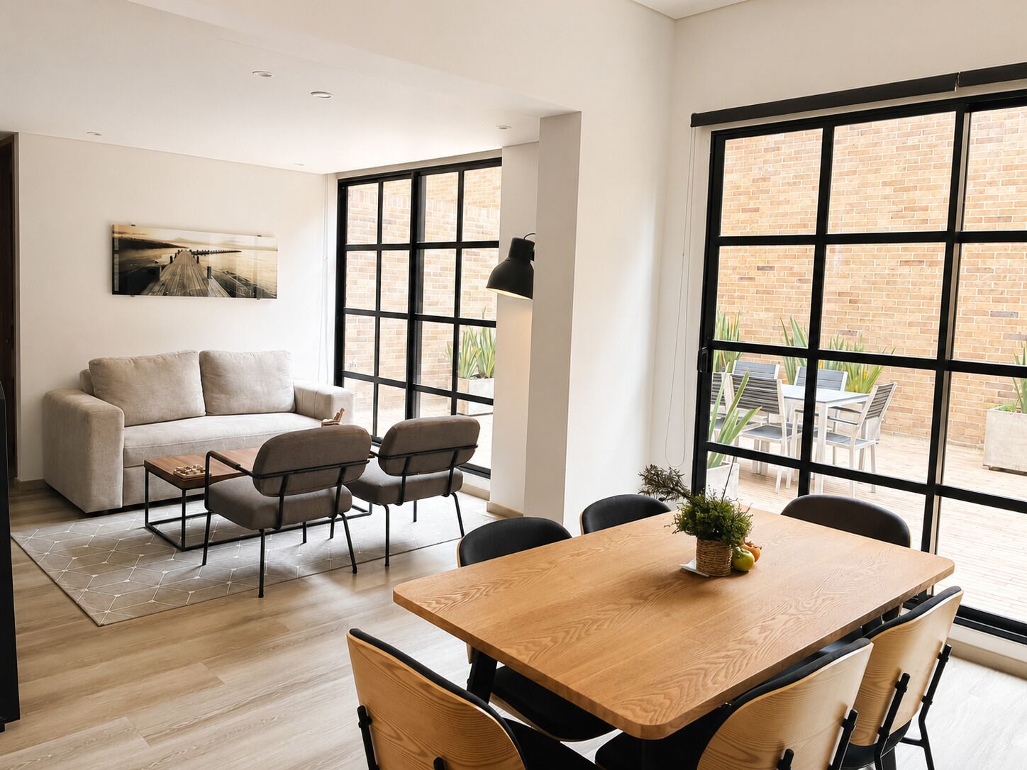 A modern living room with a sofa, chairs, a wooden table, and large windows.