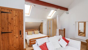 A bedroom with a bed, a sofa, and a wardrobe. There is a skylight above the bed and a window with a curtain. - The Barn - Poplar Farm (York)
