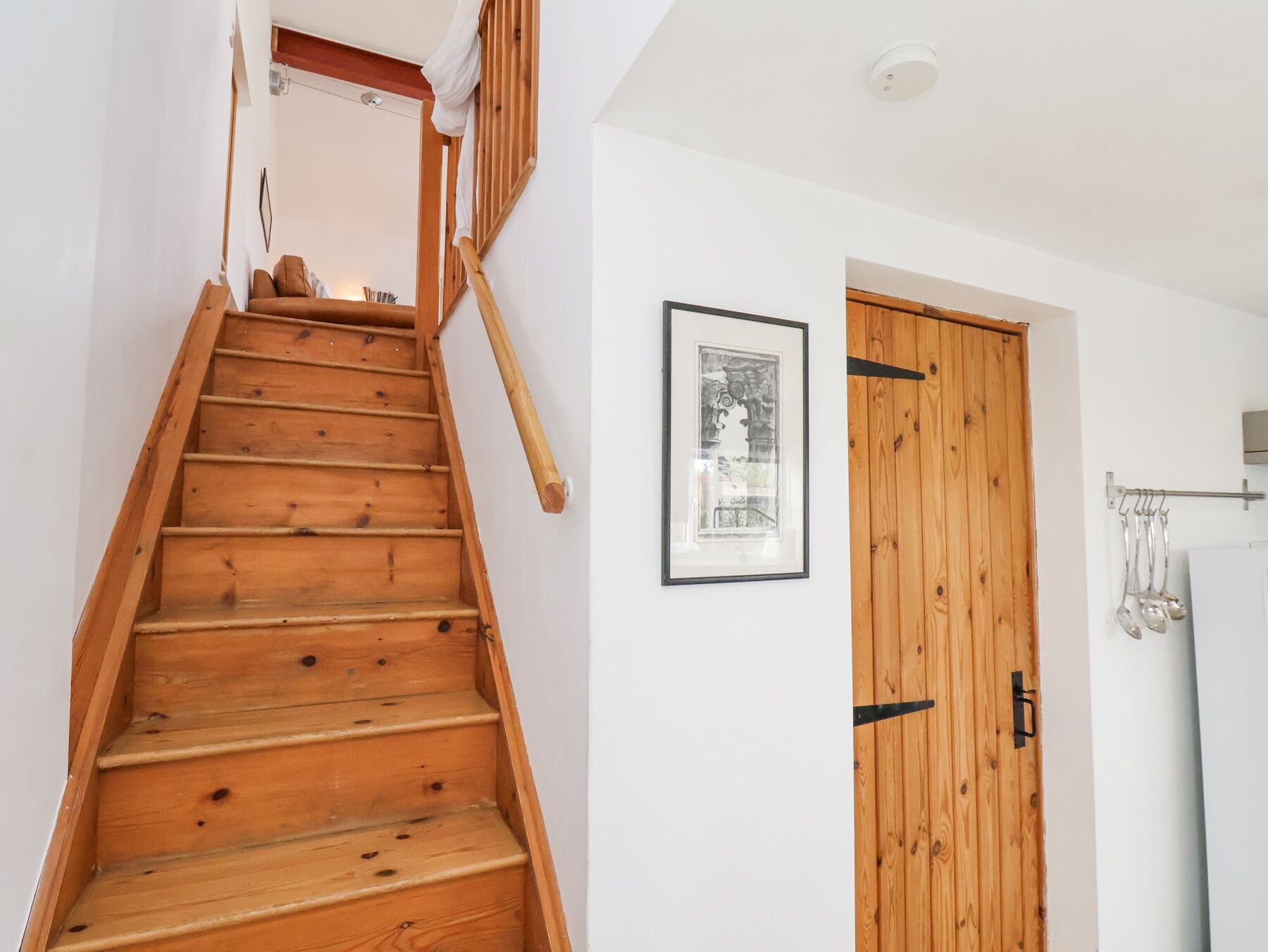 A wooden staircase leading to a room with a white wall, a framed picture, and a wooden door.