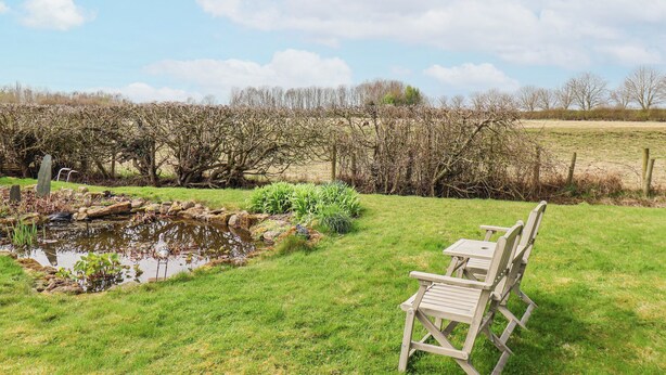 A garden with a pond, wooden chairs, and a fence. - The Barn - Poplar Farm (York)
