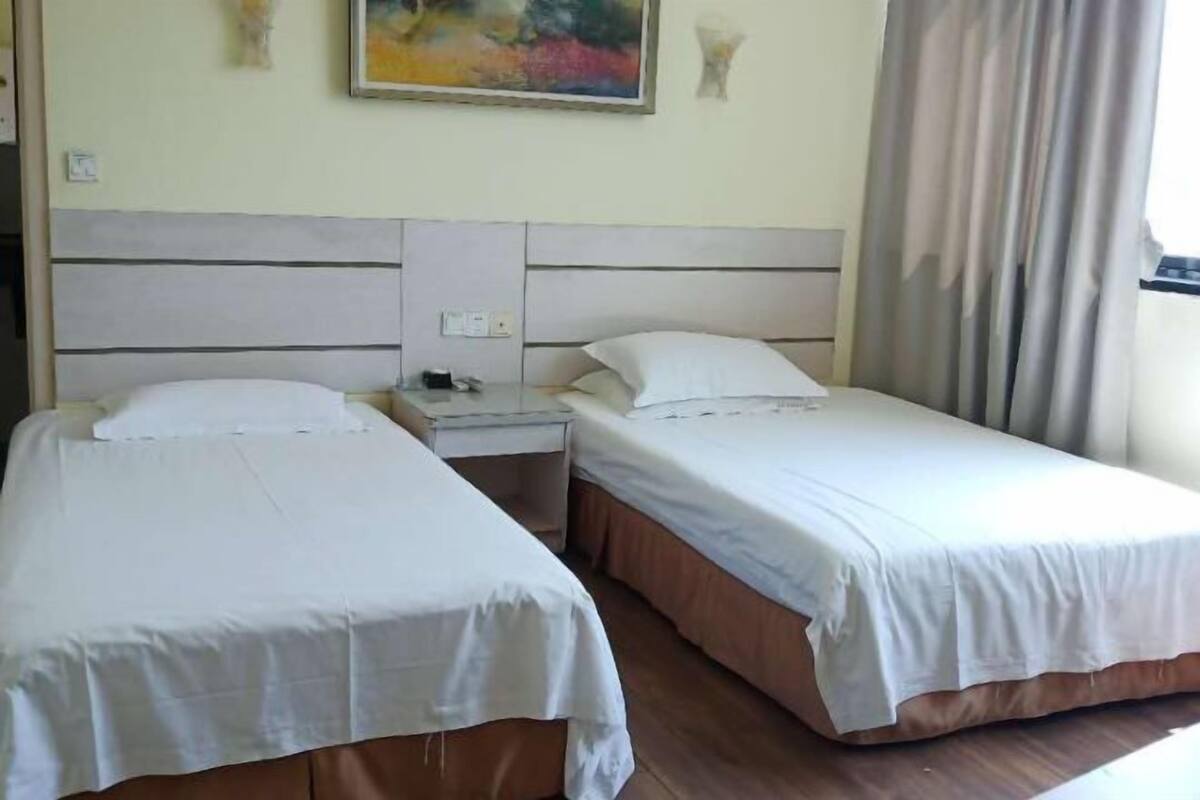 A room with two single beds, a nightstand, and a painting on the wall.