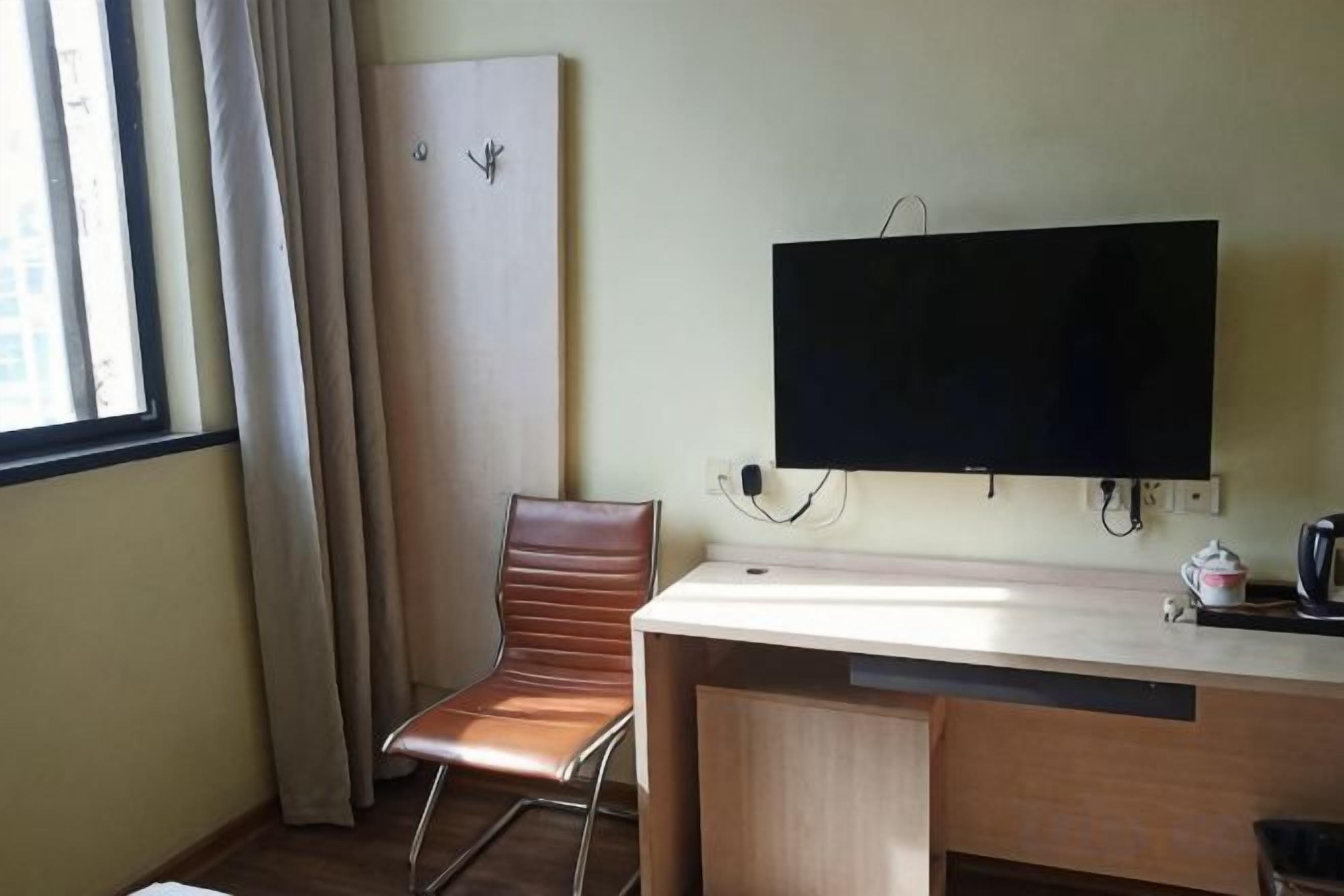 A hotel room with a desk, a chair, a television, and a window with curtains.