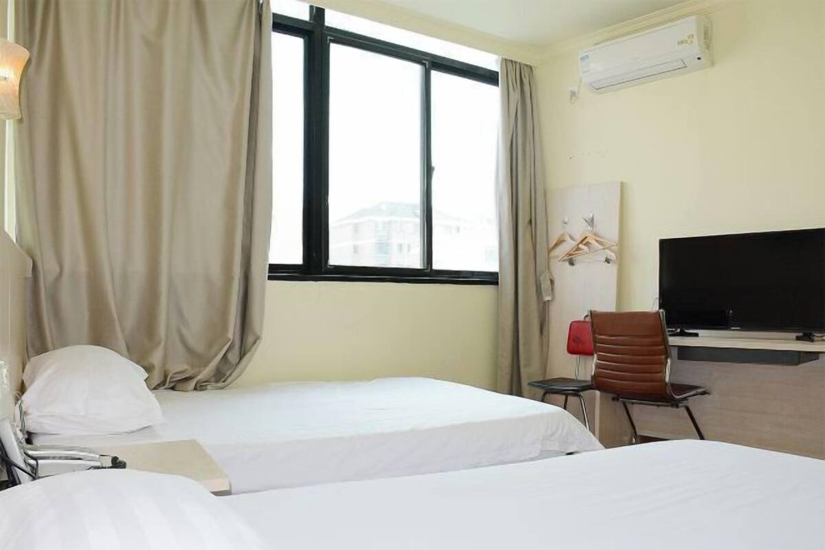 A hotel room with two beds, a TV, a desk, and a window with curtains.