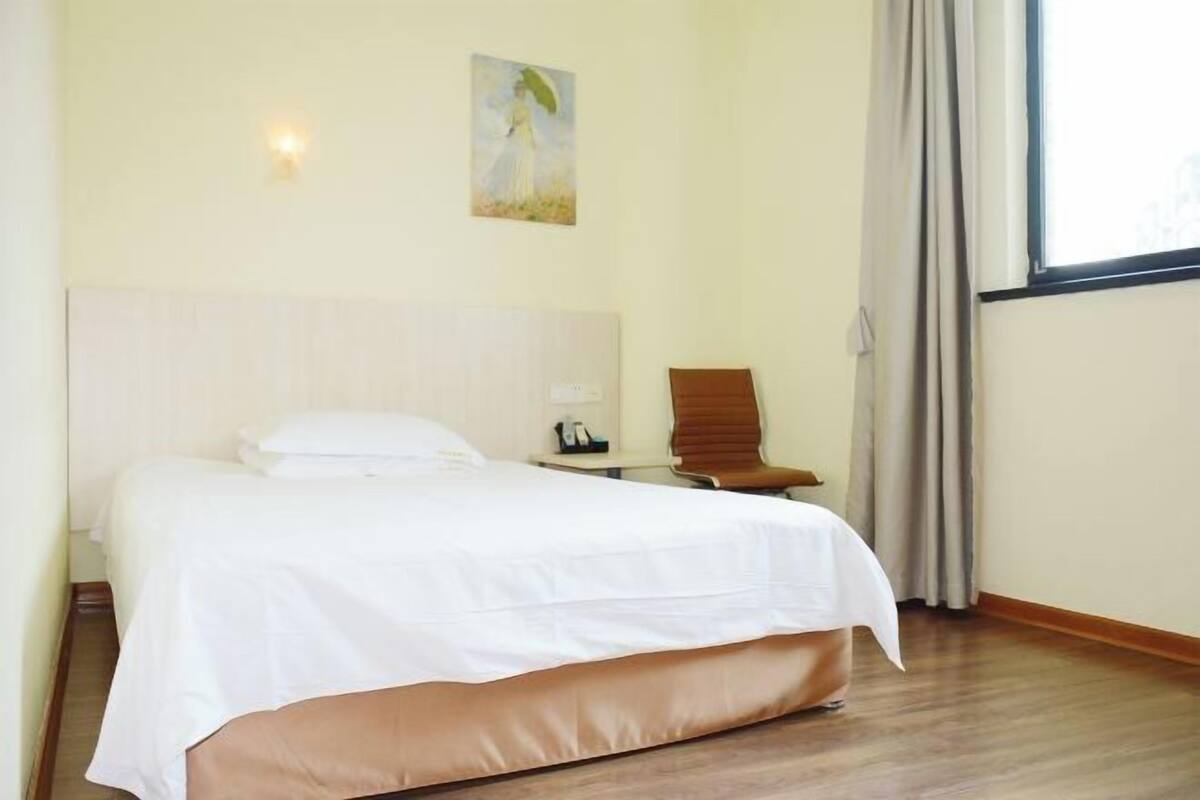 A hotel room with a bed, a chair, a painting on the wall, and a window with curtains.