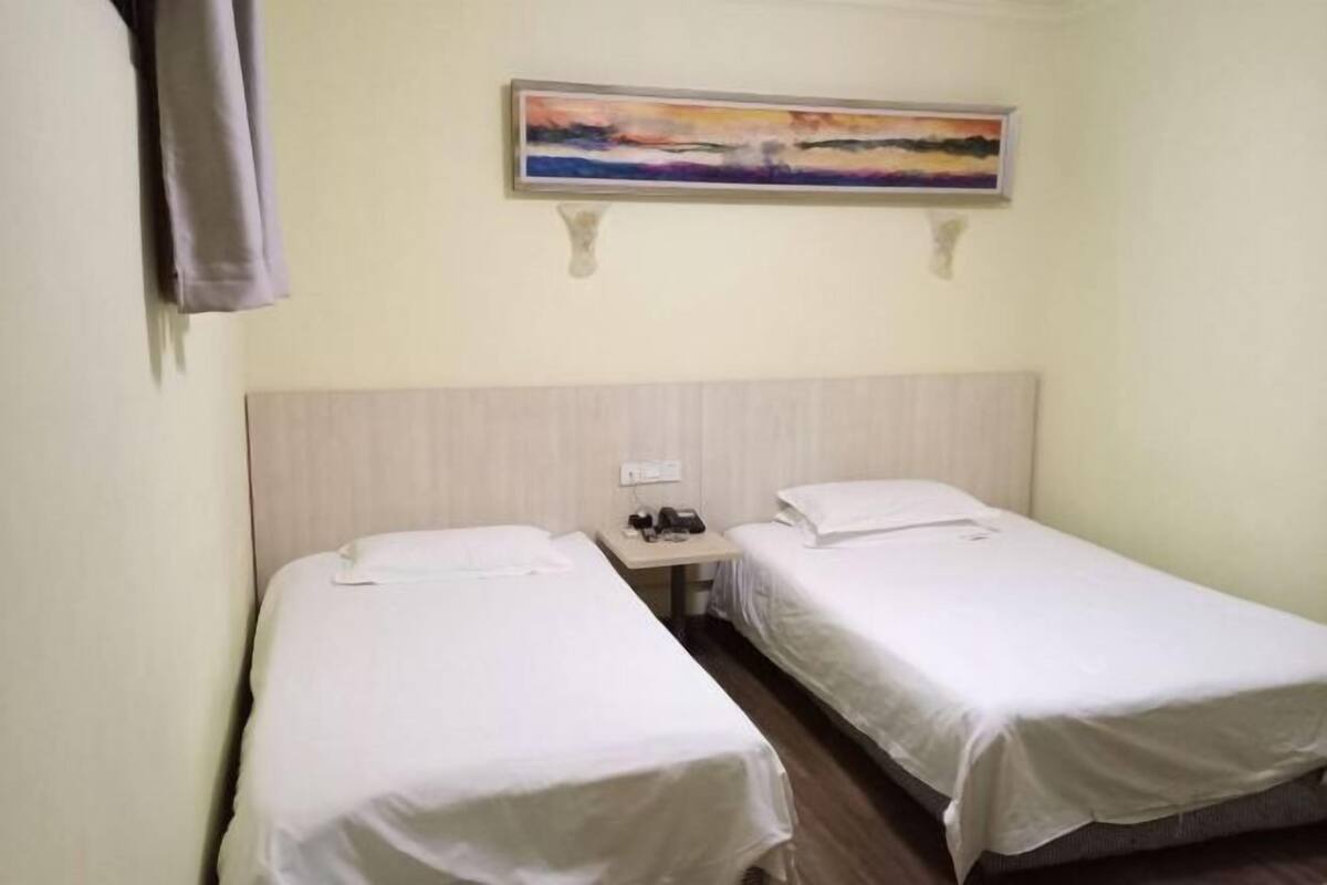 A hotel room with two single beds, a nightstand with a phone and a lamp, and a painting on the wall.