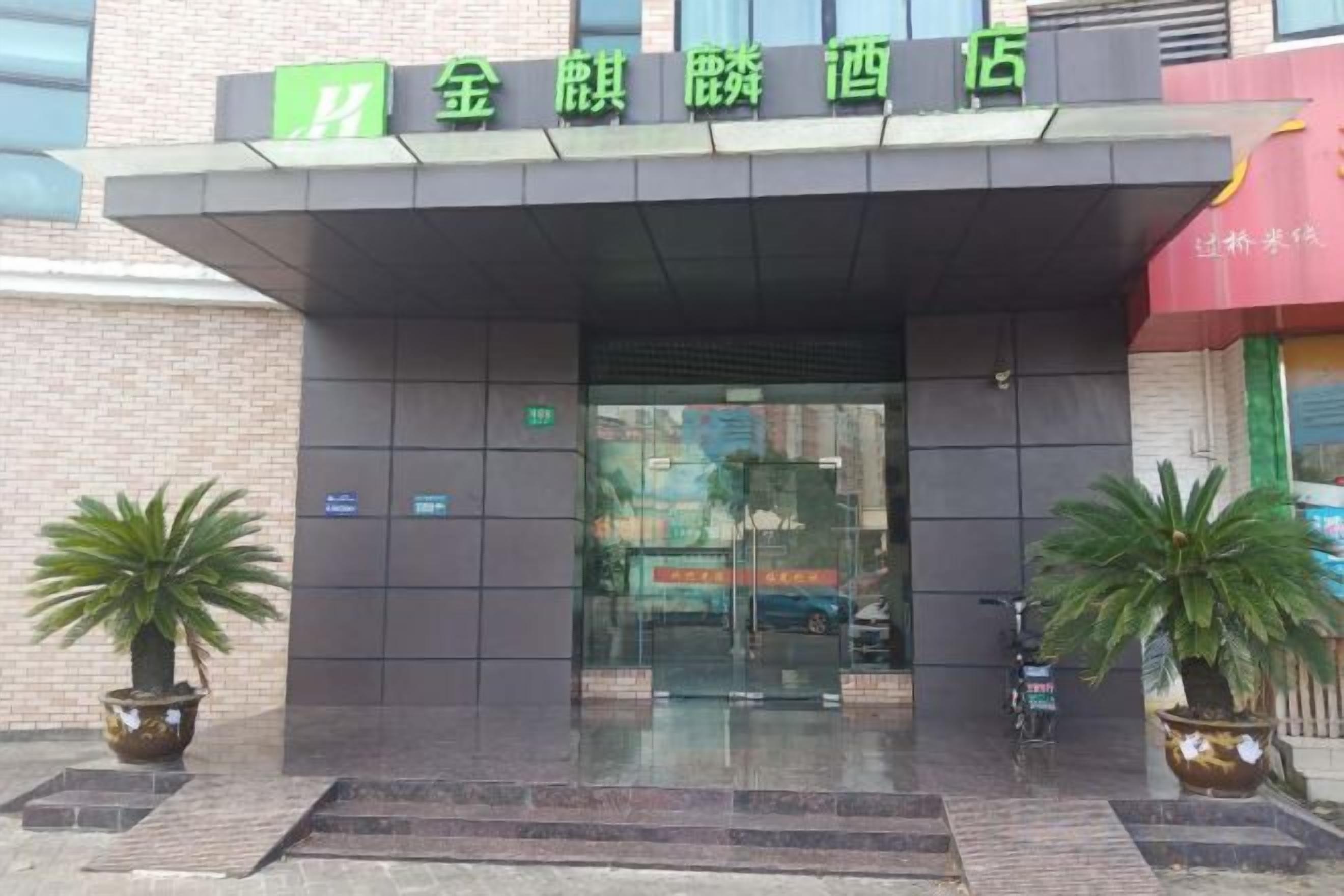 Entrada de hotel con un letrero sobre la puerta, plantas en macetas a ambos lados y puerta de vidrio transparente.
