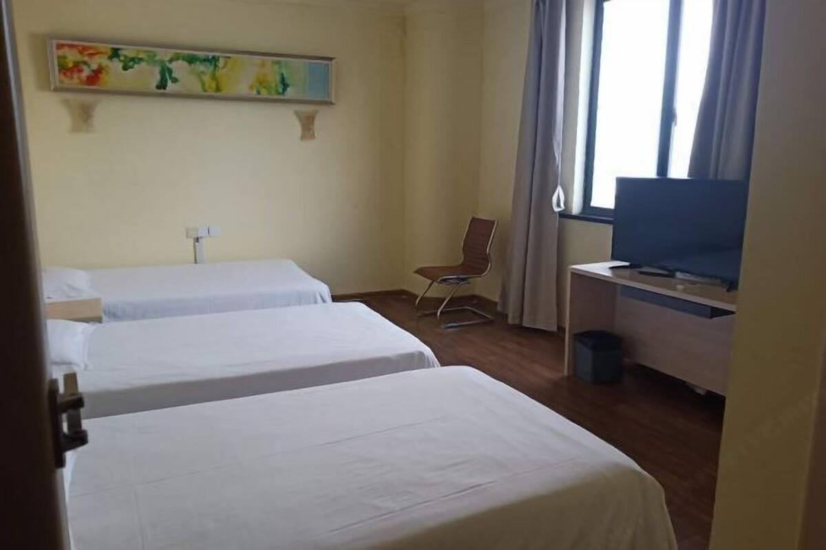 A hotel room with two single beds, a desk with a computer, a chair, and a television.