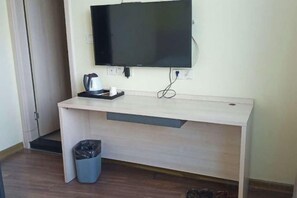 A room with a wooden desk, a television mounted on the wall, a trash bin, and a coffee maker. - Jinqilin Hotel (Shanghai Xuanqiao) (Shanghai)