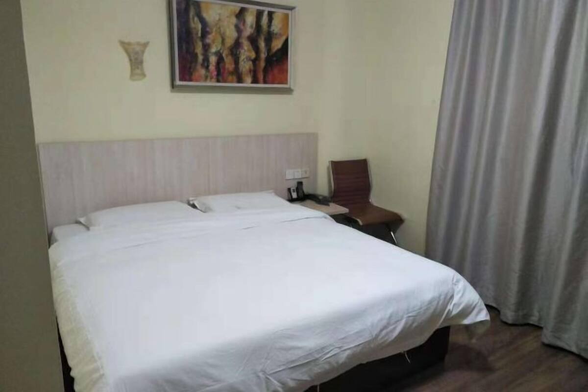 A hotel room with a large bed, a chair, a painting on the wall, and a curtain.