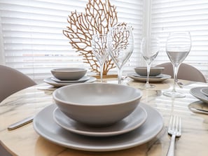 Une table à manger agrémentée d’un ensemble de bols, d’assiettes et de verres à vin, ainsi que d’un objet décoratif en corail.