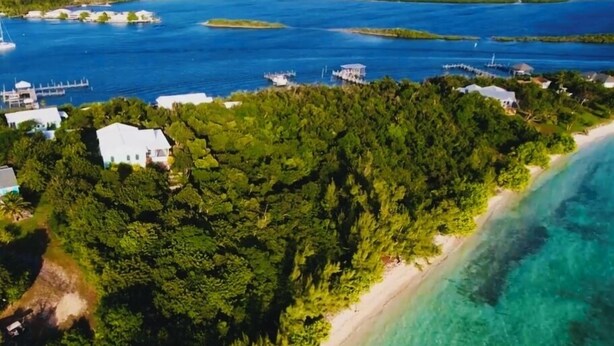 An aerial view of a coastal area with a beach, dense forest, and several buildings. - Sea Bird 3/3 Overlooking the Sea of Abaco with Private Beach & dock access (green turtle cay)
