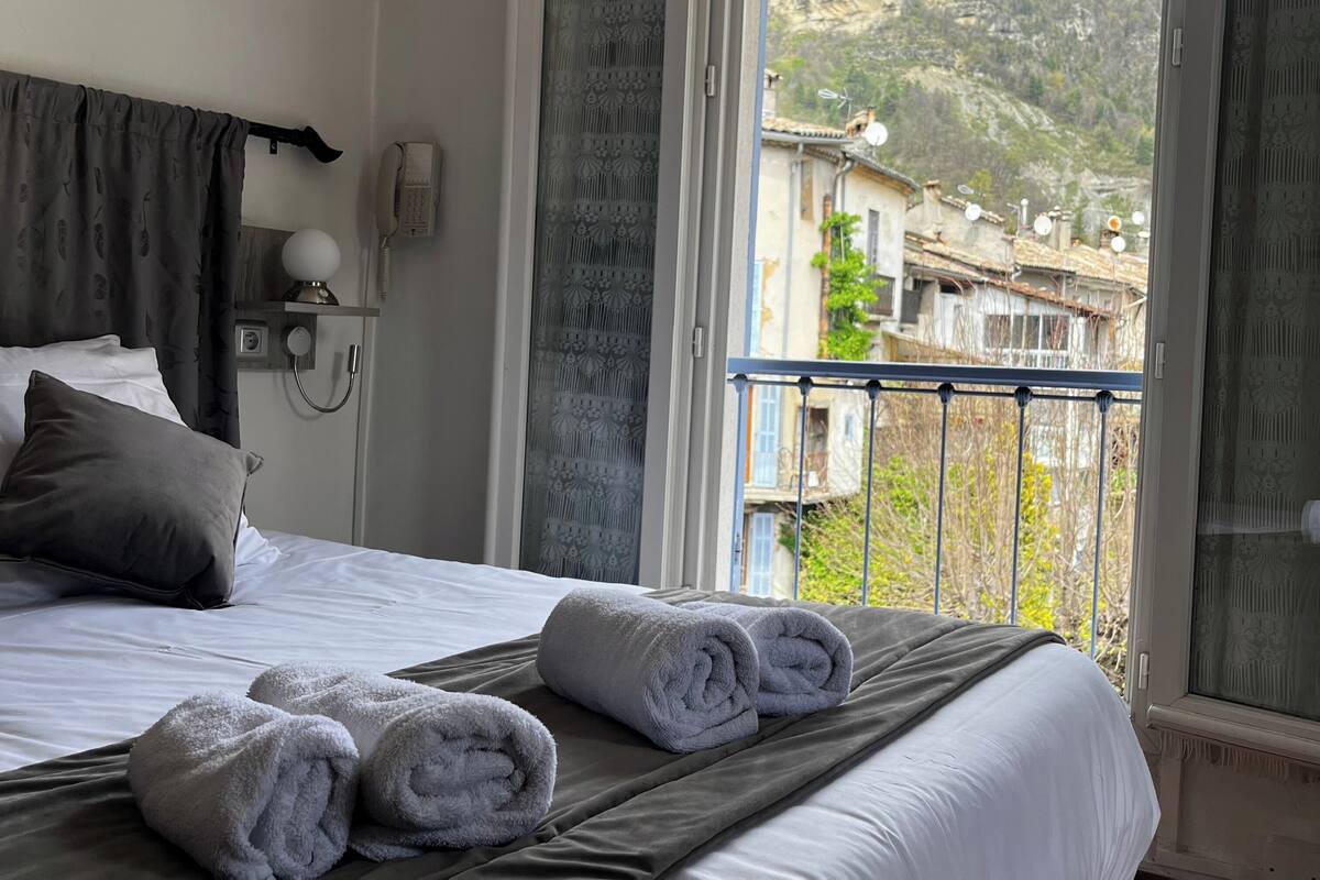A hotel room with a bed, a telephone, and a view of a mountain and buildings.