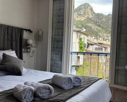 Quarto de hotel com uma cama, telefone e vista para montanhas e edifícios.