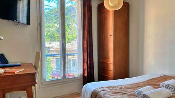 Habitación de hotel con cama, escritorio con libros, televisor y ventana con vistas a edificios.