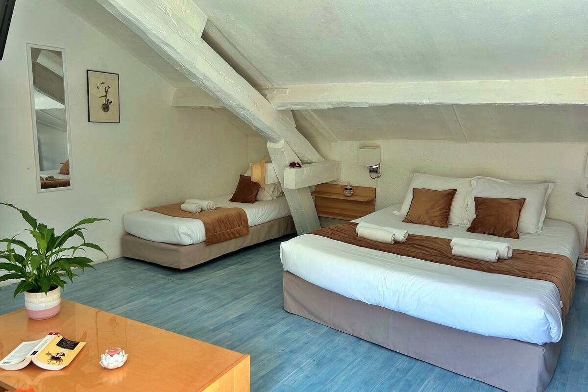 A bedroom with two beds, a bedside table, a mirror, and a potted plant.