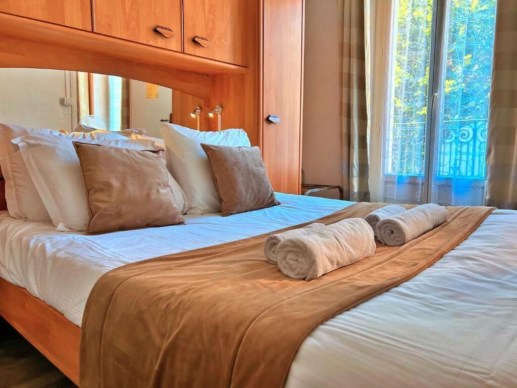 A neatly made bed with a brown bedspread and multiple pillows, a wooden headboard, and a view of a balcony with metal railings.