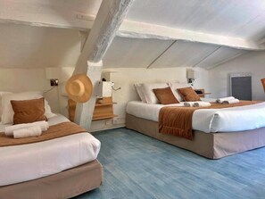 Een kamer met twee bedden, elk met witte lakens en bruine kussens, een houten hoed op een stoel, en een wit plafond met zichtbare balken.
