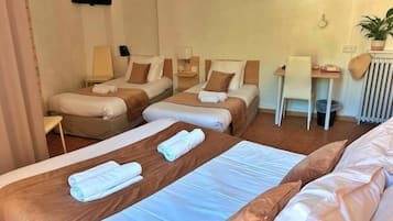 Et hotelværelse med tre senge, et skrivebord og en stol.