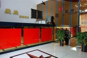 A hotel reception area with a red reception desk, a blackboard with text, and potted plants. - Aishang Hotel (Shanghai Guoquan Road) (Shanghai)