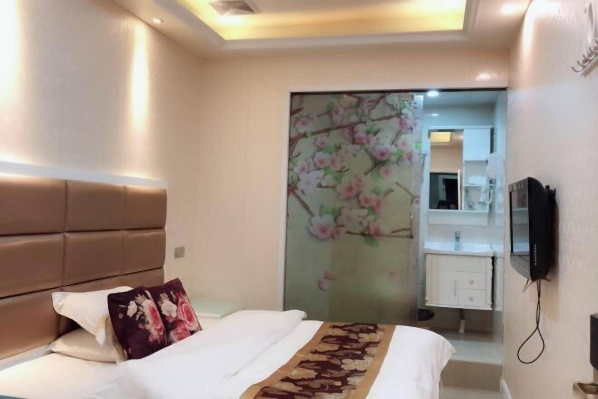 Una habitación de hotel con una cama, un espejo grande, una televisión y un adorno floral en la pared.