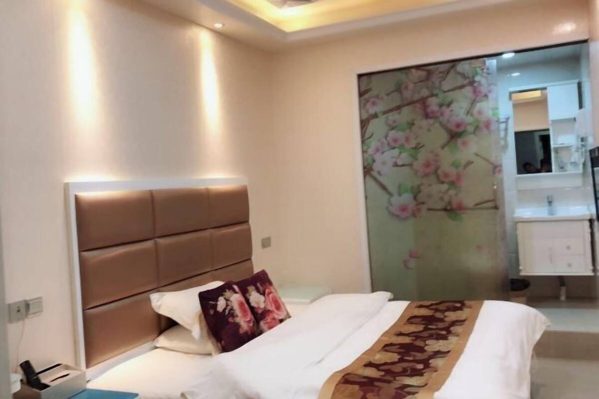 Habitación de hotel con cama, cabecero, mesita de noche, espejo y baño con lavabo y espejo.