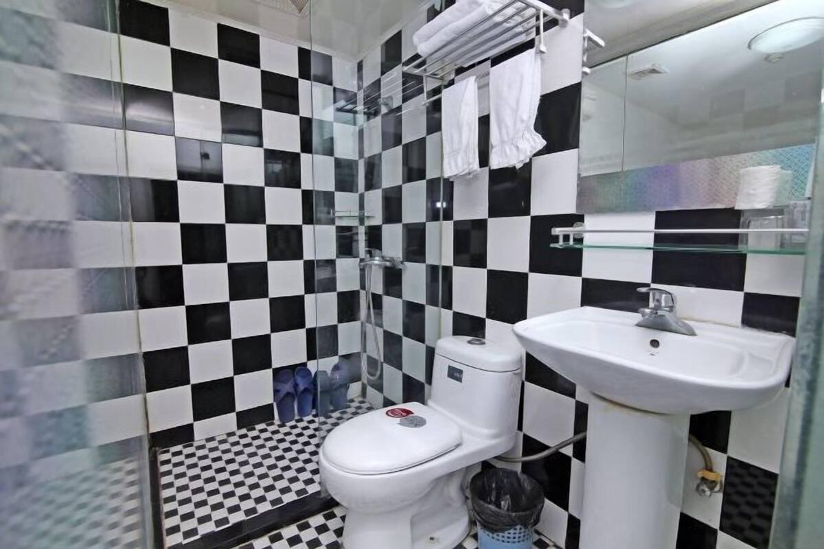 Un baño con piso a cuadros, inodoro, lavamanos y cabina de ducha de vidrio.