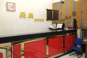 A reception desk with a black counter, red panels, and a blue chair. There is a framed sign with Chinese characters and a menu board above the counter. - Aishang Hotel (Shanghai Guoquan Road) (Shanghai)