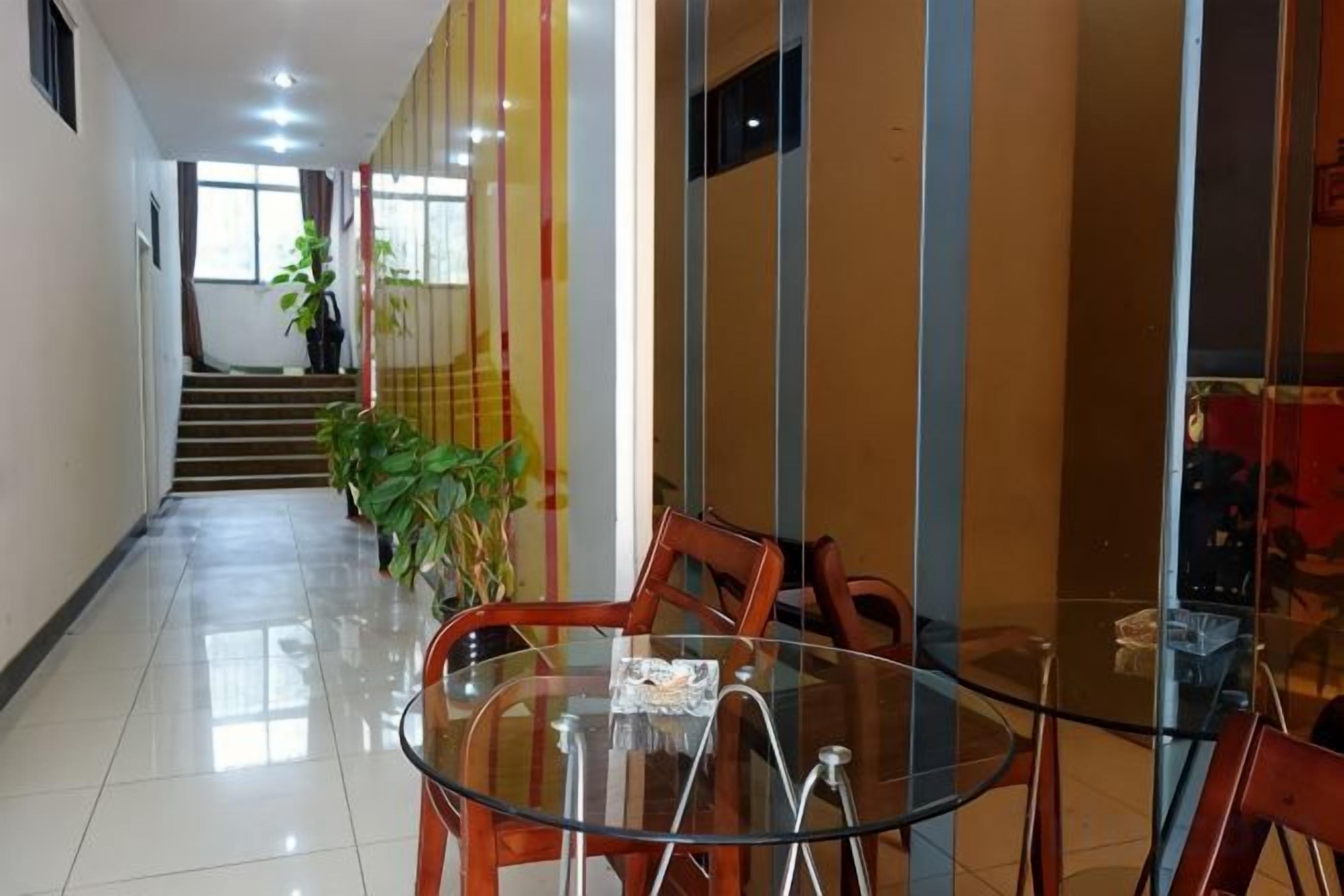 Un hall de hotel con una mesa de vidrio, sillas, una escalera y plantas en macetas.