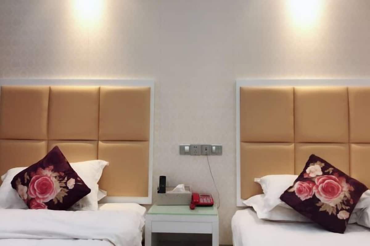 Habitación de hotel con dos camas, cada una con cabecero, mesita de noche con teléfono y caja de pañuelos.