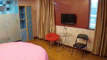 A bedroom with a bed, a TV, a wardrobe, and a small table with chairs.