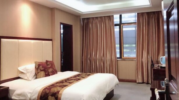 A hotel room with a large bed, a headboard, a window with curtains, and a door. - Aishang Hotel (Shanghai Guoquan Road) (Shanghai)