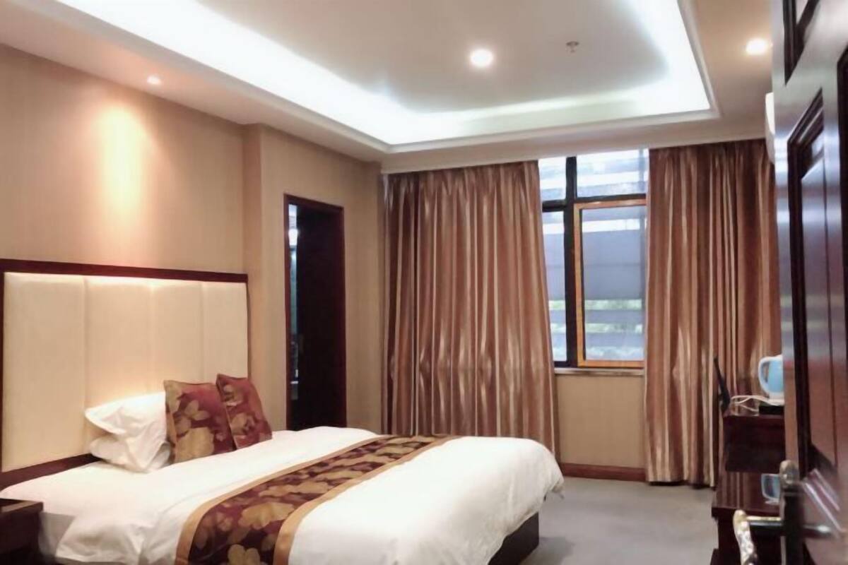 Una habitación de hotel con una cama grande, un cabecero, una ventana con cortinas y una puerta.