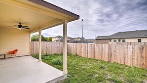 Ein überdachter Patio-Bereich mit Deckenventilator, Holzpforte und Rasengrundstück.