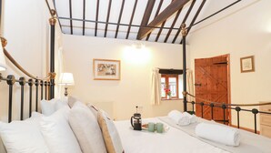 A four-poster bed with a wooden ceiling, a bedside table with a lamp, and a window with curtains. - Pear Tree (Dereham)