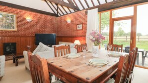A dining area with a brick wall, wooden ceiling beams, a television, and a table set for four. - Pear Tree (Dereham)