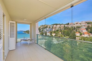 A balcony with a view of a coastal town, a bed, and a window with blinds. - Hedera Estate, Hedera A58 (Dubrovnik)