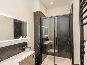 Un baño moderno con ducha envuelta en vidrio, lavamanos blanco y pared con azulejos de mármol.