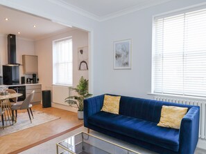Una sala de estar moderna con un sofá azul, una mesa de centro de vidrio y un comedor con una mesa y sillas blancas.