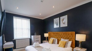 A bedroom with a large bed, bedside tables, a dresser, a radiator, and a window with blinds. - The Salisbury - 1 Bedroom Deluxe Apartment (Scarborough)