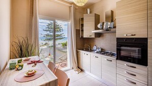 A modern kitchen with a view of the sea, featuring a dining area with a table set for two, a gas stove, and wooden cabinets. - Villa Marena by Villa Plus (Santa Maria del Focallo)