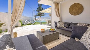 A covered outdoor seating area with a sofa, a wicker coffee table, and a bowl of fruit. - Villa Marena by Villa Plus (Santa Maria del Focallo)