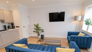 A modern living room with two blue sofas, a coffee machine, a potted plant, and a flat-screen TV on the wall. - The Salisbury 1 Bed Classic Apartment (Scarborough)