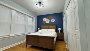 Une chambre à coucher avec un lit en bois, une literie blanche, un mur d’accent bleu, un luminaire au plafond et une armoire à plusieurs portes.