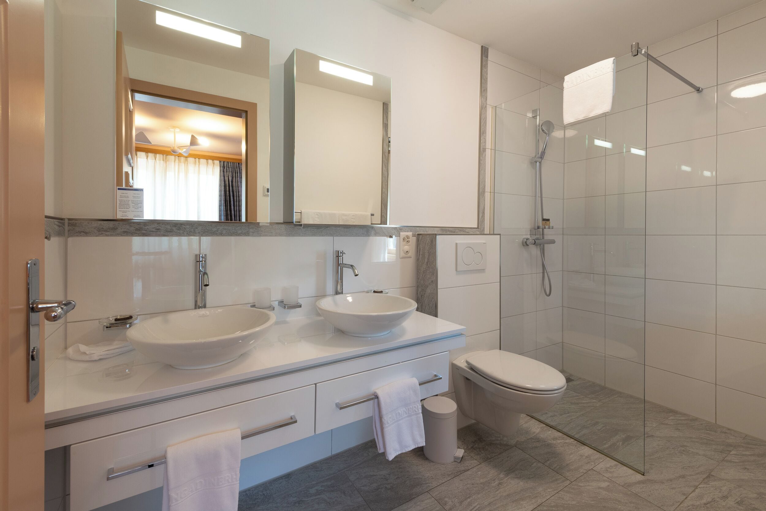 A modern bathroom with two sinks, a toilet, and a glass-enclosed shower.