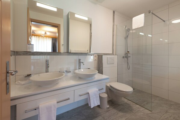 Un baño moderno con dos lavamanos, un inodoro y una ducha con cerramiento de vidrio.