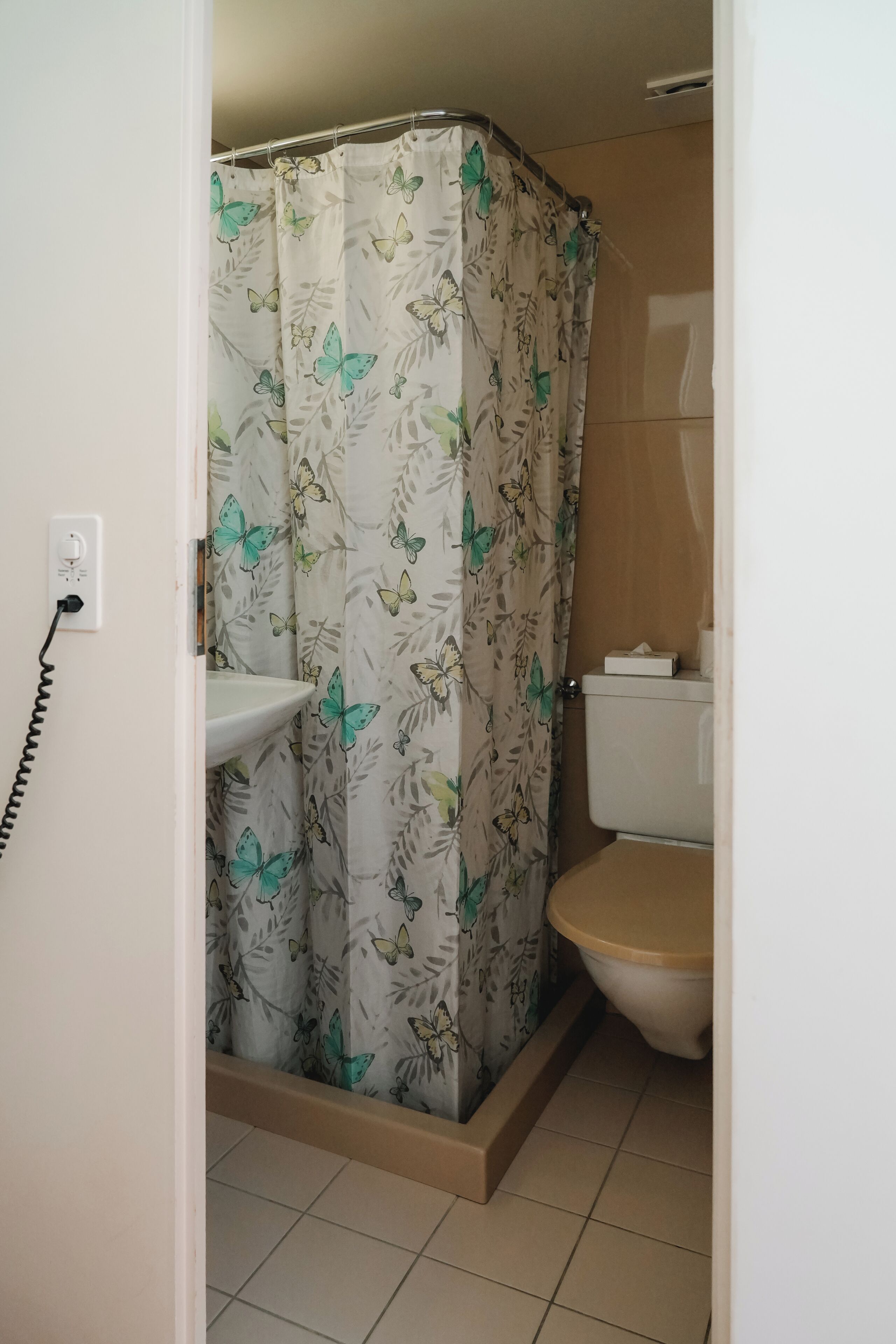 Un baño con cortina de ducha con estampado de mariposas, un inodoro y un lavabo con toma de corriente.